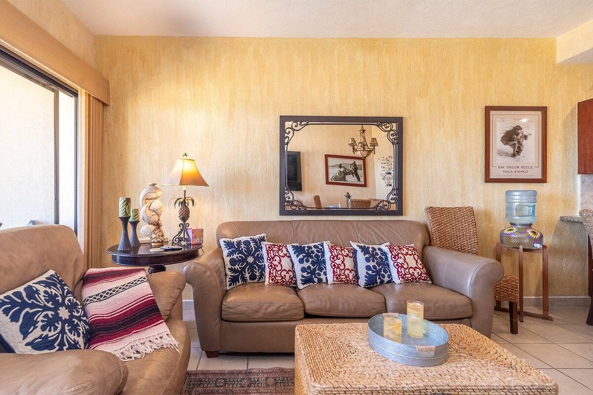 A cozy living room with a brown leather sofa, a coffee table with candles, and a large mirror on the wall.