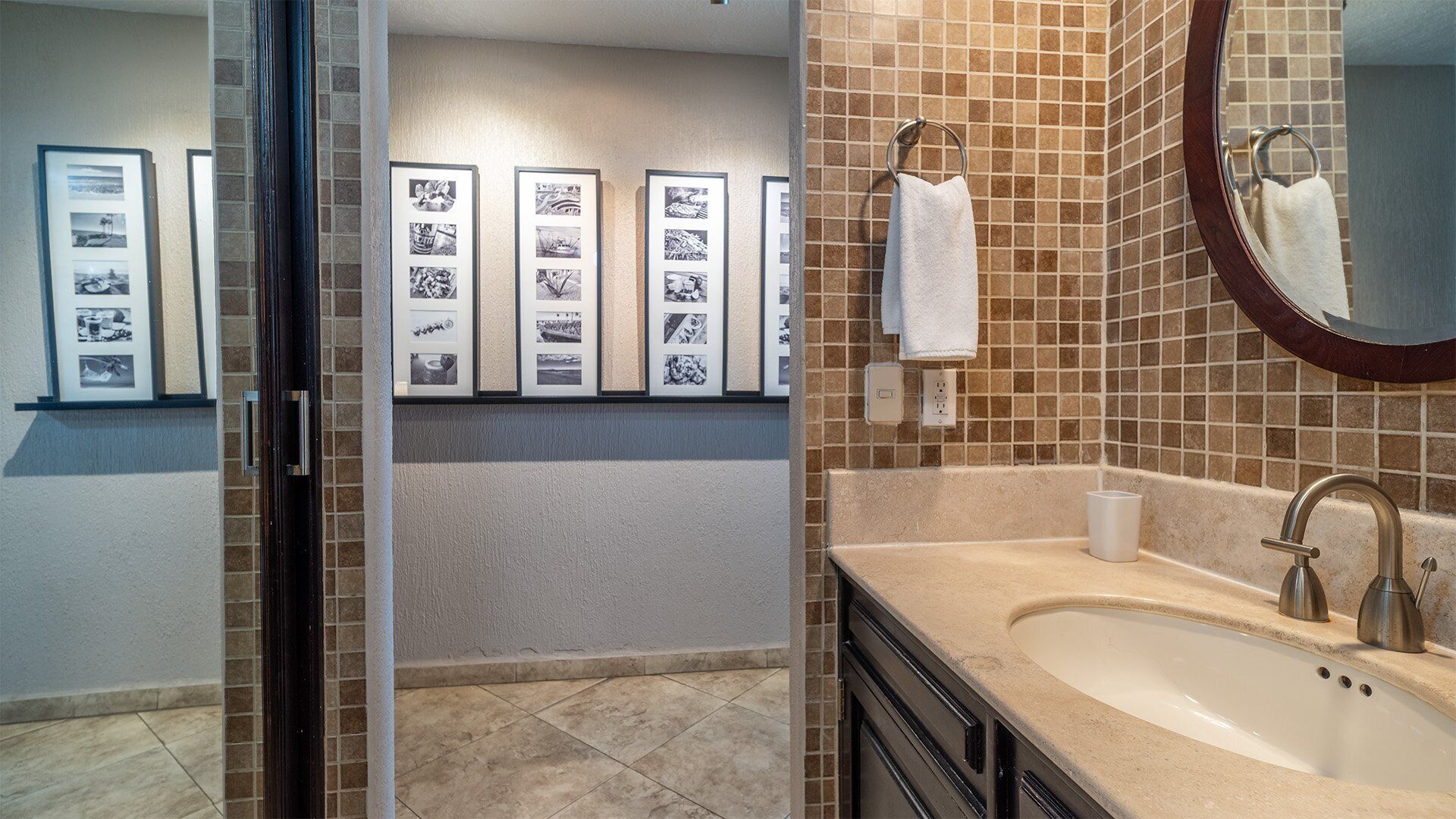 Une salle de bain avec un lavabo, un miroir et des murs carrelés. Des tableaux encadrés sont accrochés au mur.