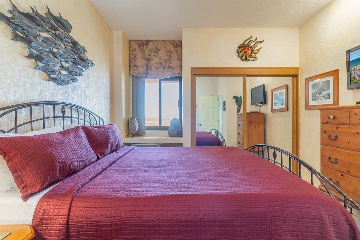 Une chambre à coucher comprenant un lit, une commode, un tableau décoratif et une porte donnant sur une autre pièce.