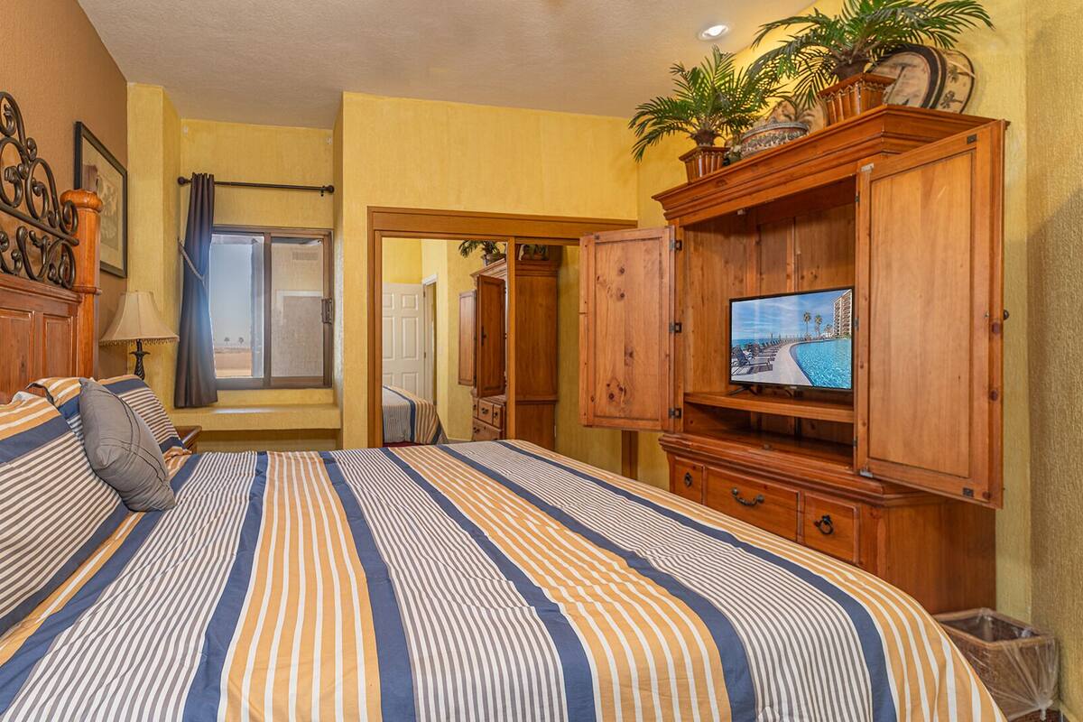 Een hotelkamer met een groot bed, een houten hoofdbord, een televisie op een houten kast en een raam met gordijnen.