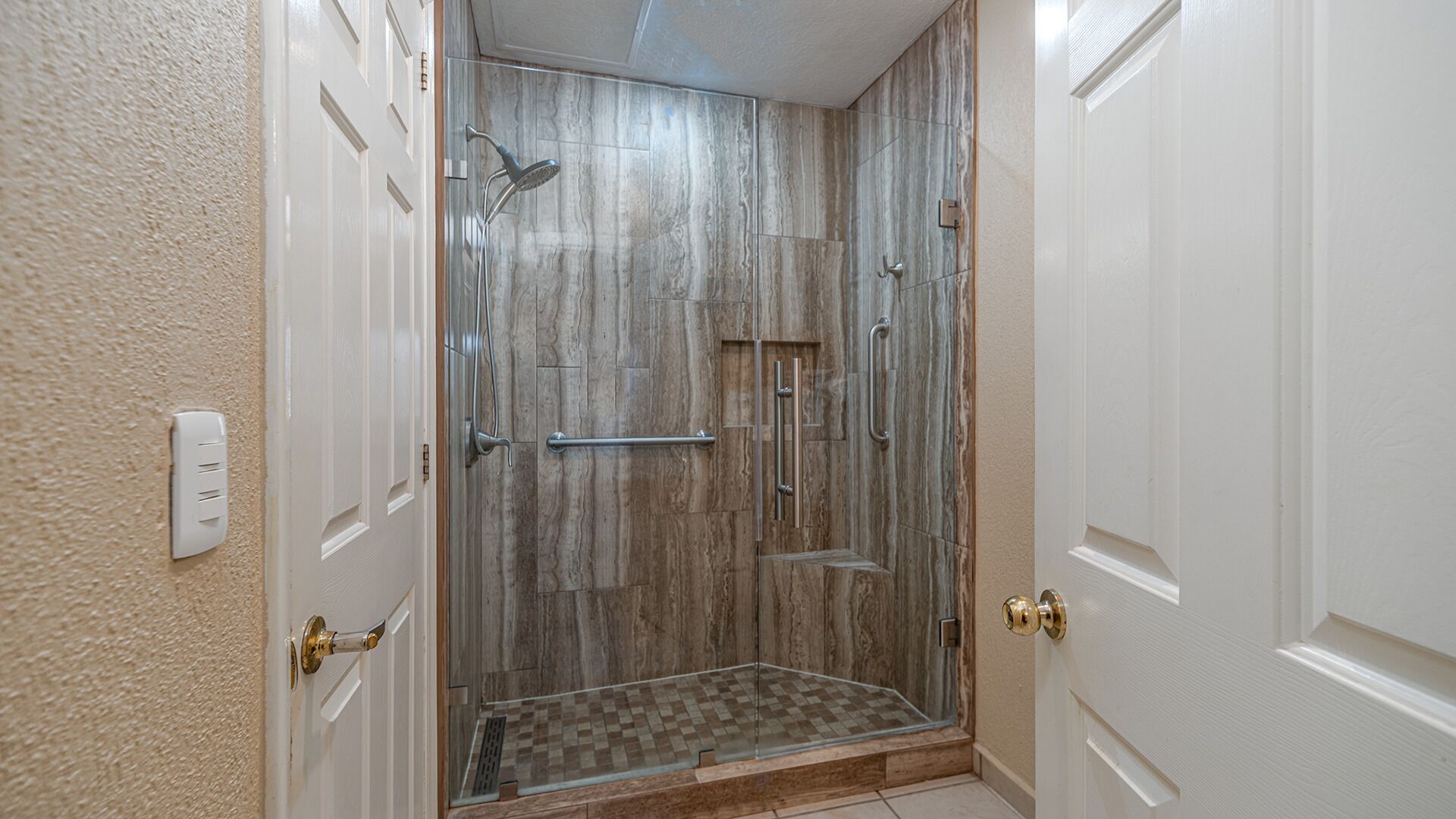 A walk-in shower with a glass door, a showerhead, and a handrail.