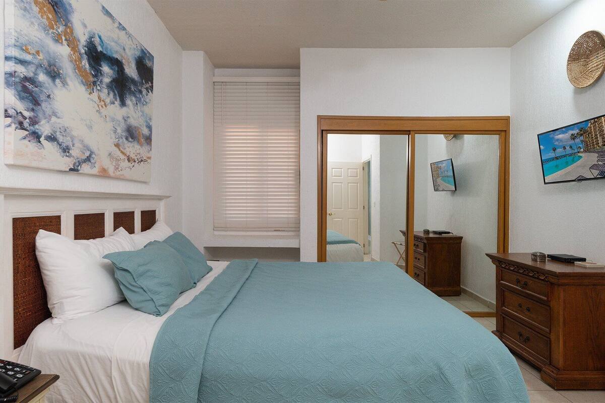Een slaapkamer met een bed, een dressoir, een spiegel en kunstwerken aan de muur.