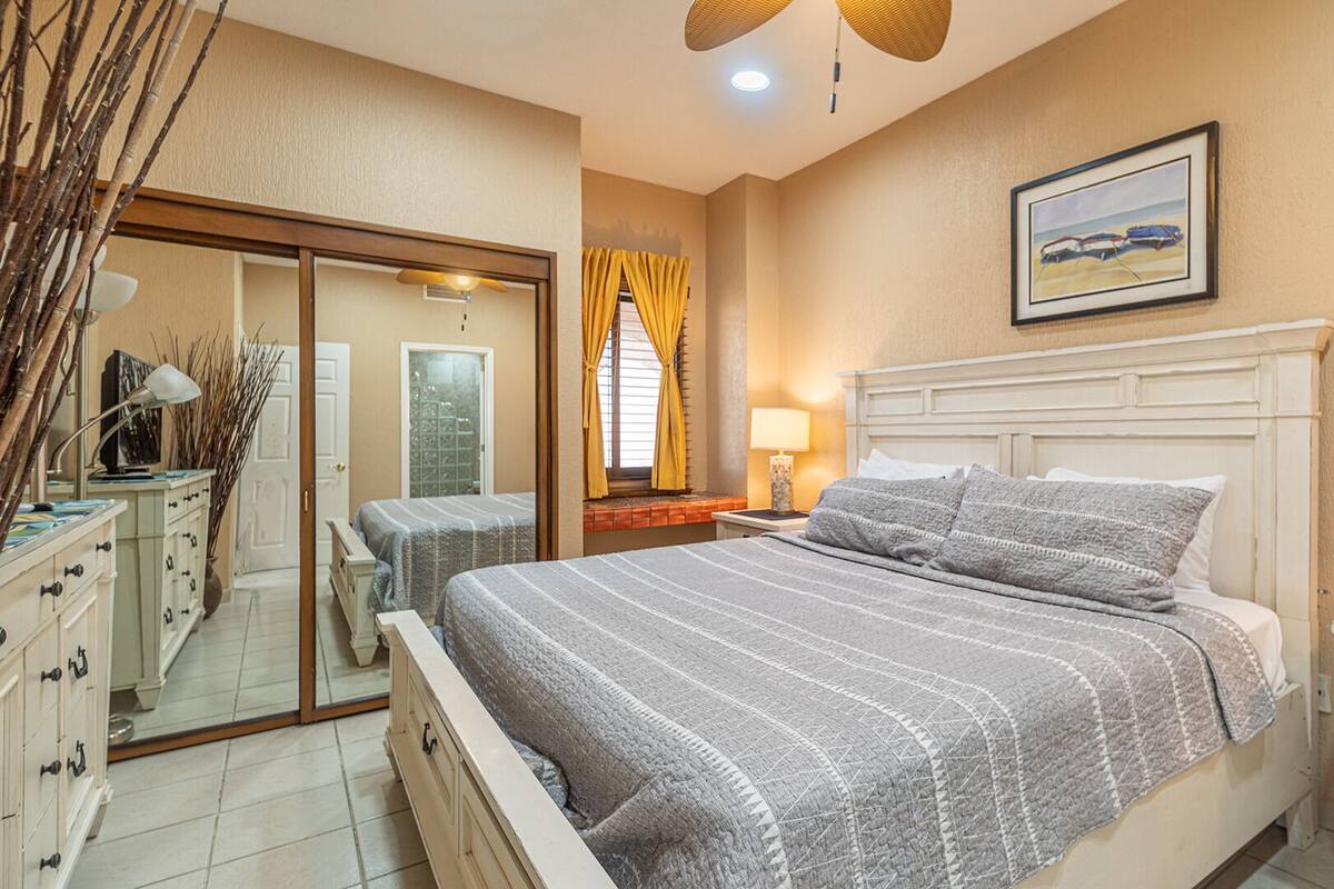 Een slaapkamer met een bed, nachtkastjes, een spiegel en een raam met gordijnen.