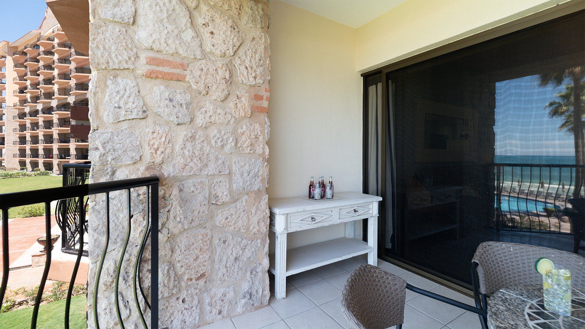 A balcony with a stone wall, a white console table, and two wicker chairs.