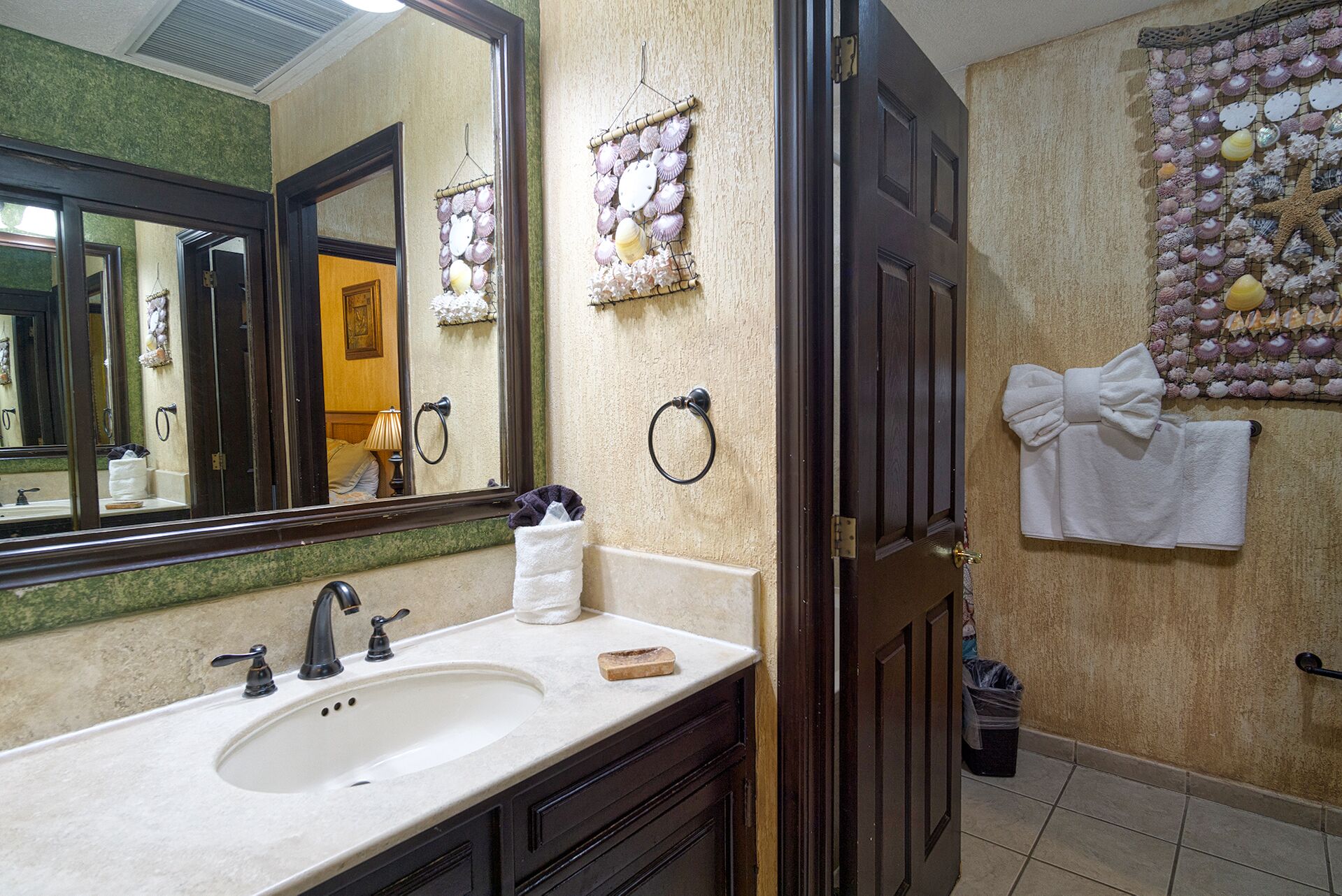 A bathroom with a large mirror, two sinks, a towel rack, and a decorative wall with shells.