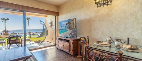 A dining area with a view of a beach and pool, a television, and a dining table set with plates and cups.