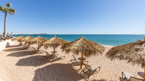 Una playa con filas de tumbonas y sombrillas de paja, una palmera y una vista despejada del océano.