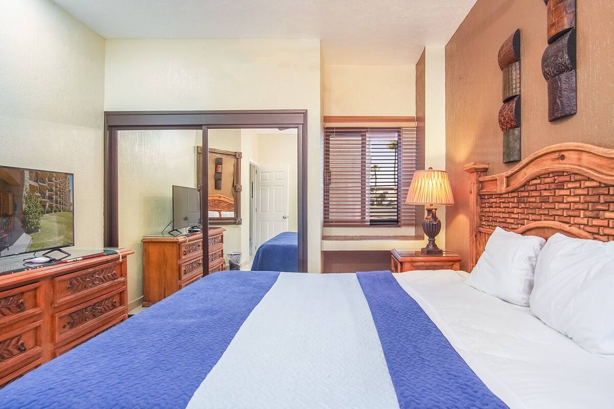 Een hotelkamer met een groot bed, een televisie, een dressoir en een raam met jaloezieën.