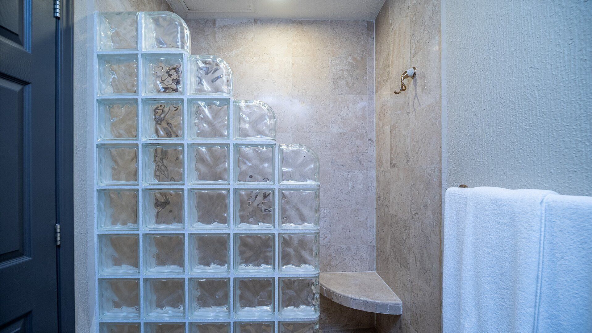 A bathroom with a glass shower enclosure, a white towel, and a stone countertop.