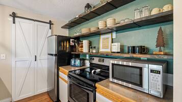A kitchen with a refrigerator, stove, microwave, and wooden countertop.