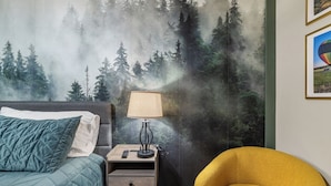 Une chambre à coucher avec un lit, une table de chevet avec une lampe, une chaise et une fresque murale sur le thème de la forêt.