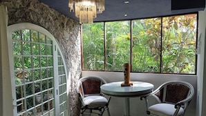 A room with a round table and two chairs, a large arched window with a view of greenery, and a chandelier.