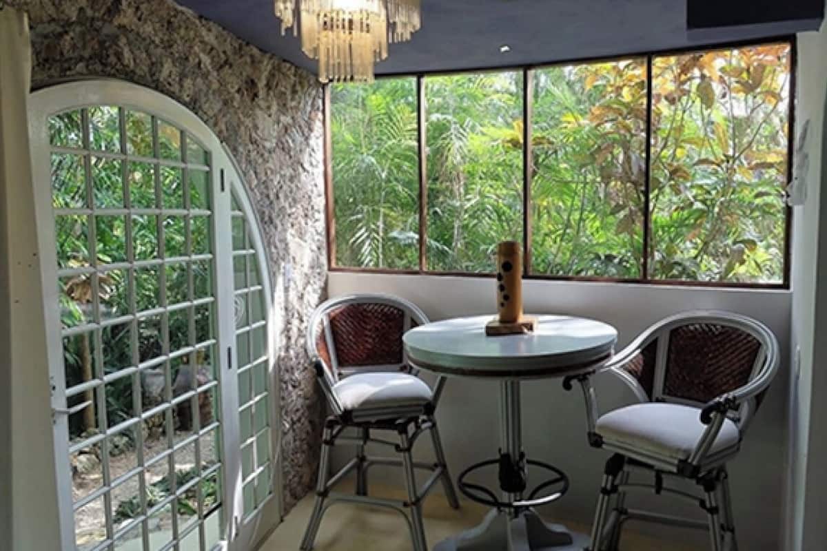 A room with a round table and two chairs, a large arched window with a view of greenery, and a chandelier.