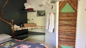 A bedroom with a bed, a wooden branch, a shelf with towels, a fan, and a decorative door.
