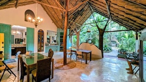 A spacious dining area with a high thatched roof, a bar area, and a view of lush greenery outside.