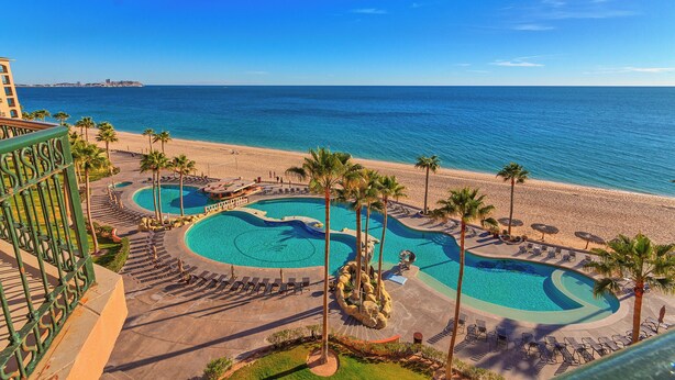 Ein Resort mit großzügigem Poolbereich, Palmen und Blick auf den Strand.
