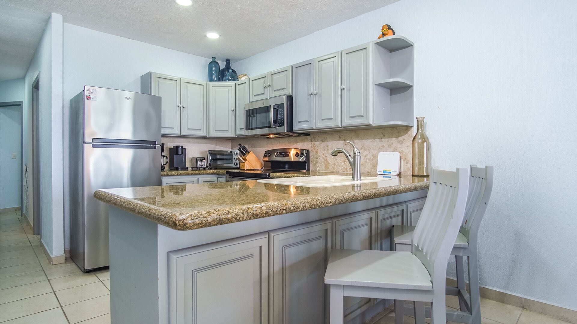 Cozinha compacta com geladeira, micro-ondas, fogão e um pequeno espaço de refeições com uma cadeira.