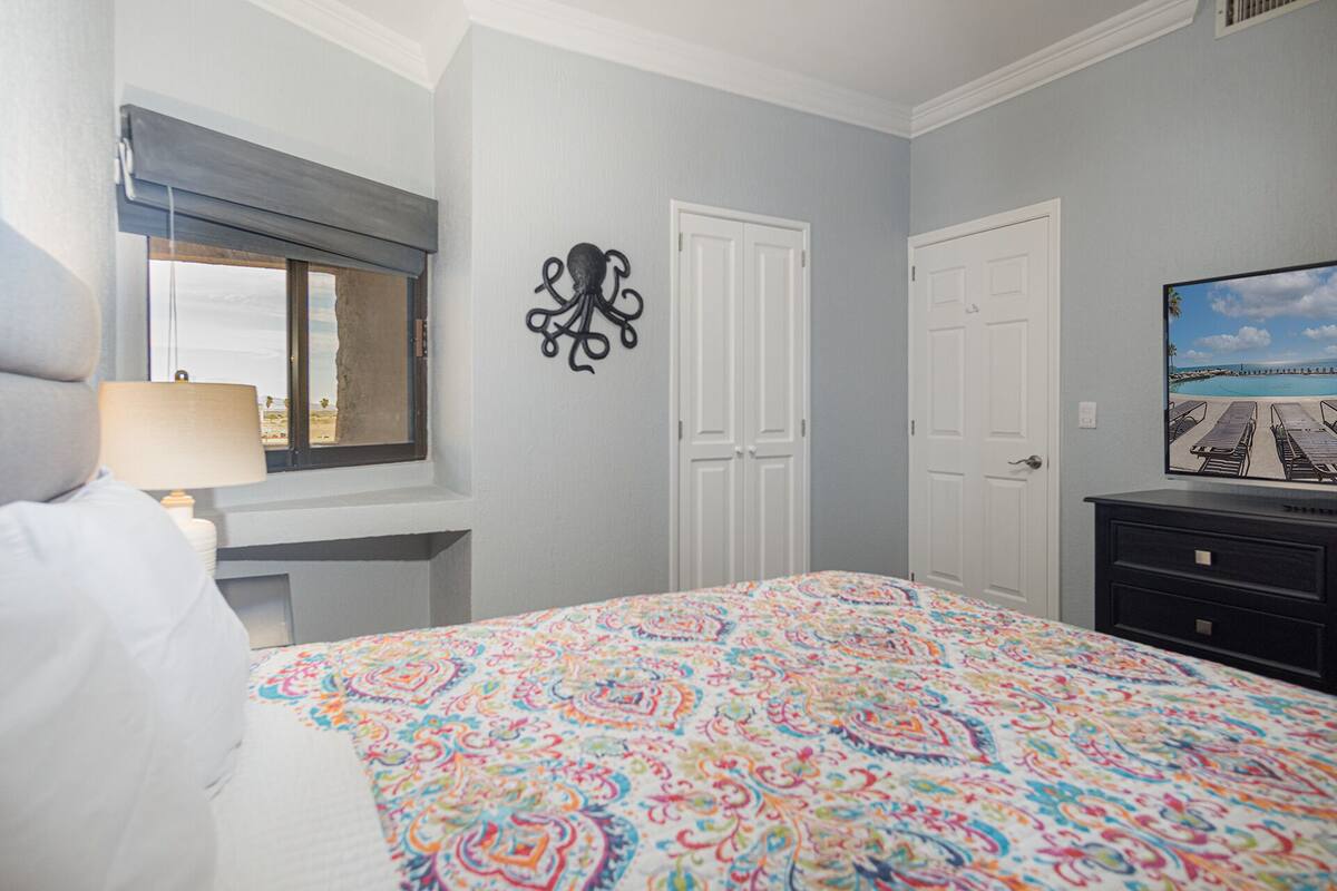 Een slaapkamer met een bed, een kaptafel, een raam met uitzicht en een kunstwerk aan de muur.