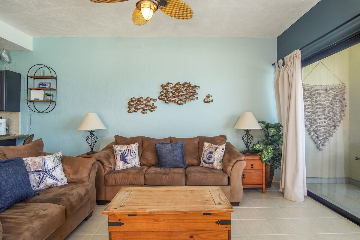 A living room with a brown sofa set, two side tables with lamps, a wooden coffee table, and a decorative wall piece.