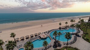 A resort with a large pool area, palm trees, and a beach view.
