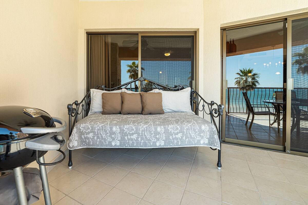 Ein Bett mit gemustertem Überwurf, ein kleiner Tisch mit Stuhl und ein Grill.