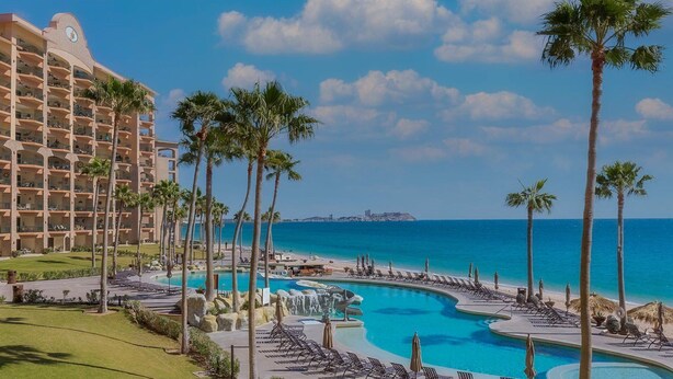 A resort with a large pool, palm trees, and a view of the ocean.