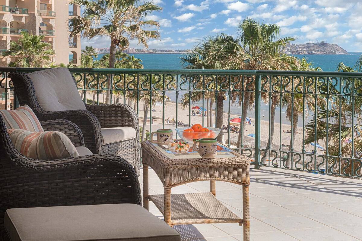 Ein Balkon mit Korbmöbeln, einem kleinen Tisch mit Dekoration und Blick auf Strand und Meer.