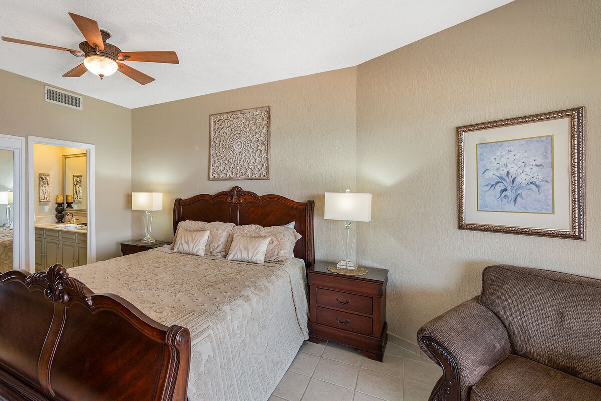 A hotel room with a large bed, two bedside tables, a ceiling fan, a mirror, and a framed picture on the wall.