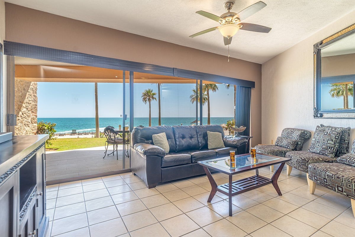 A spacious living area with a view of the ocean, a ceiling fan, and a large mirror.