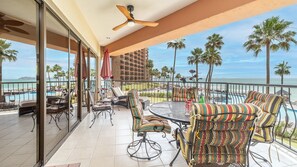 Ein Balkon mit Blick auf den Strand, ausgestattet mit gestreiften Stühlen und einem runden Tisch, der einen Pool und ein Hotelgebäude überblickt.