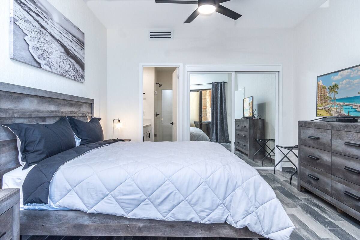 Ein Schlafzimmer mit einem Bett, einem Schminktisch, einem Deckenventilator und einem Bild an der Wand.