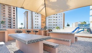 Eine Außenpatio-Terrasse mit Grillmöglichkeit, einer Kinderspielanlage und Blick auf umliegende Gebäude.