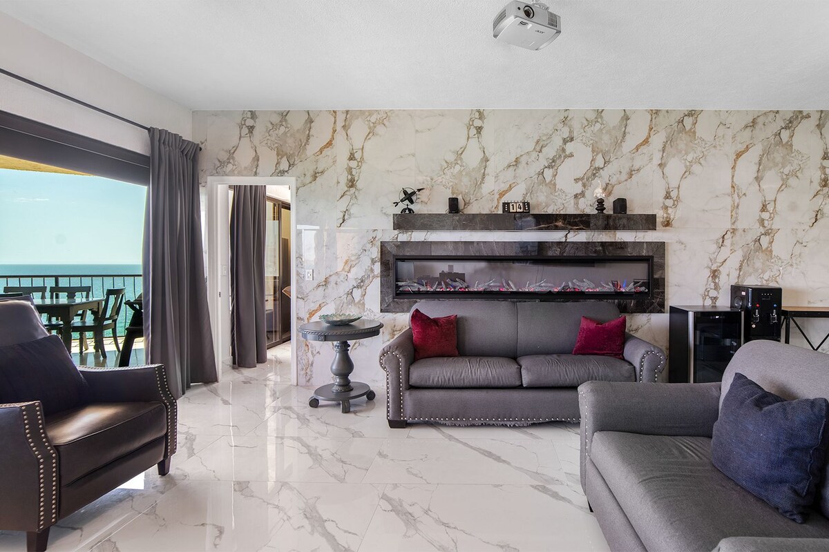 A modern living room with a marble wall, a sofa, a coffee table, and a balcony with a view.