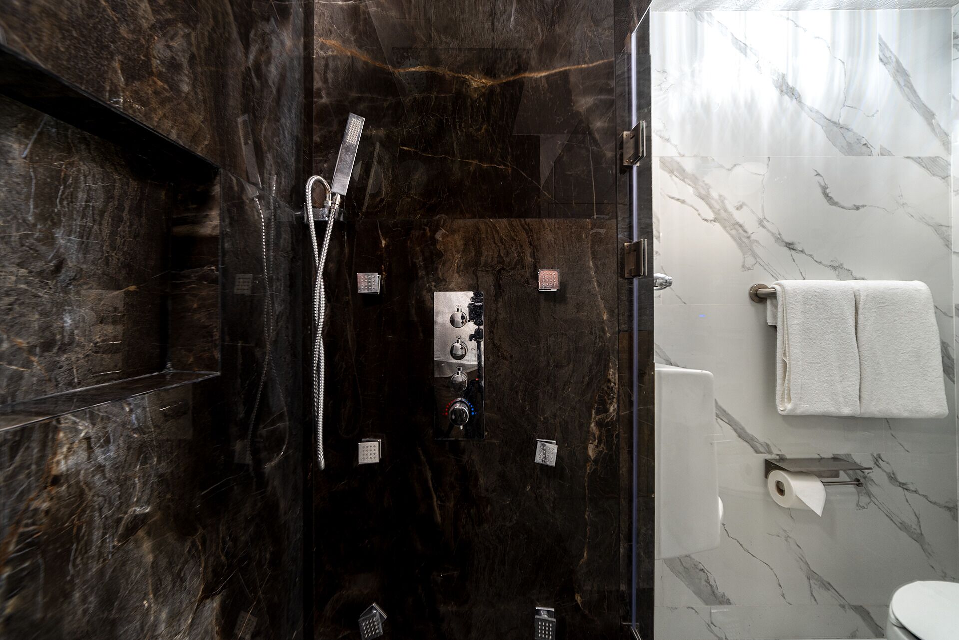 Ein modernes Badezimmer mit einer schwarzen Marmerdusche, einer weißen Toilette und einer Marmorwand.