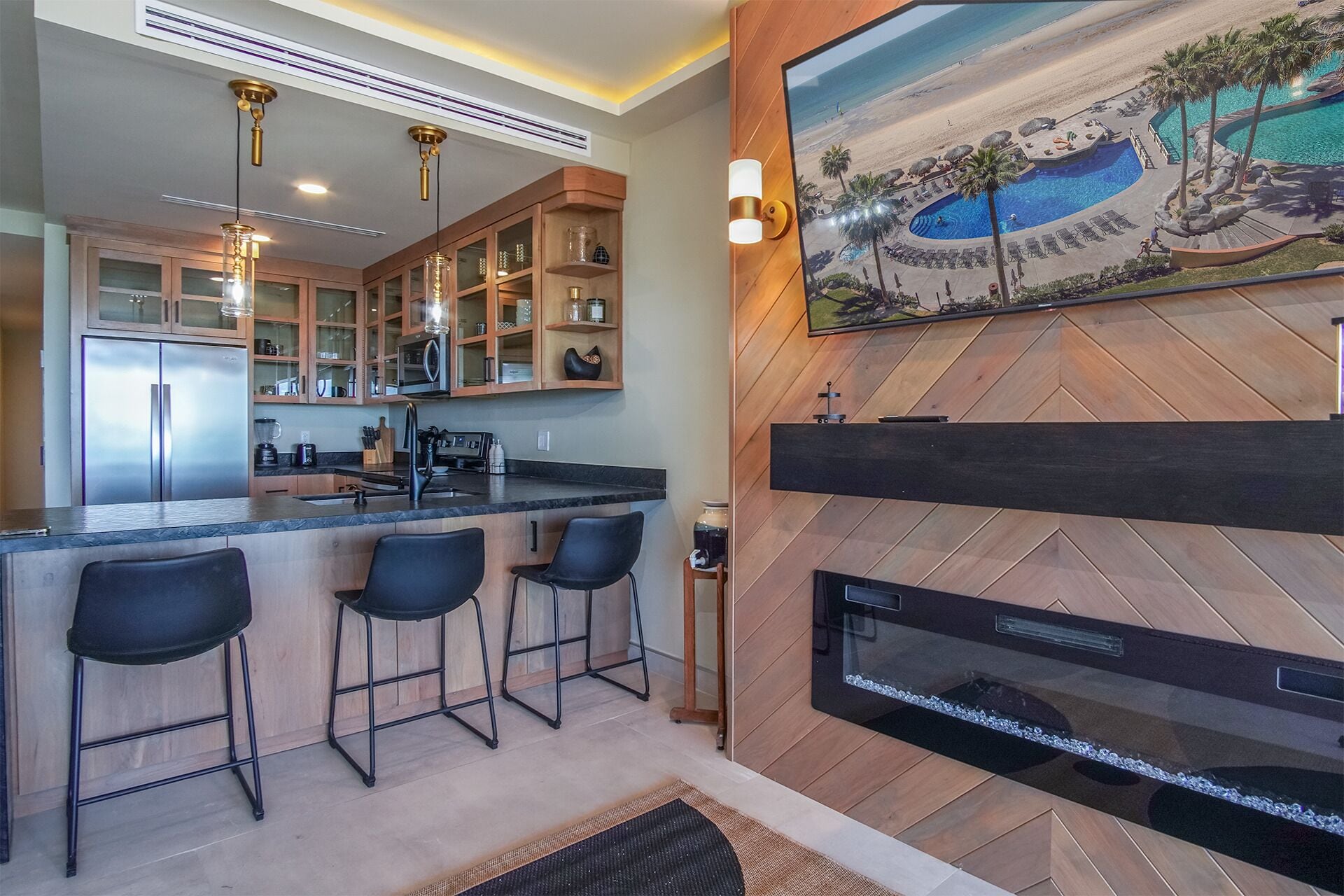 A modern kitchen with a bar area, a fireplace, and a large beach view painting.