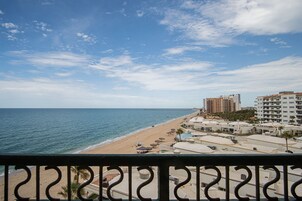 A beach view with a clear sky, a sandy shore, and buildings in the background.