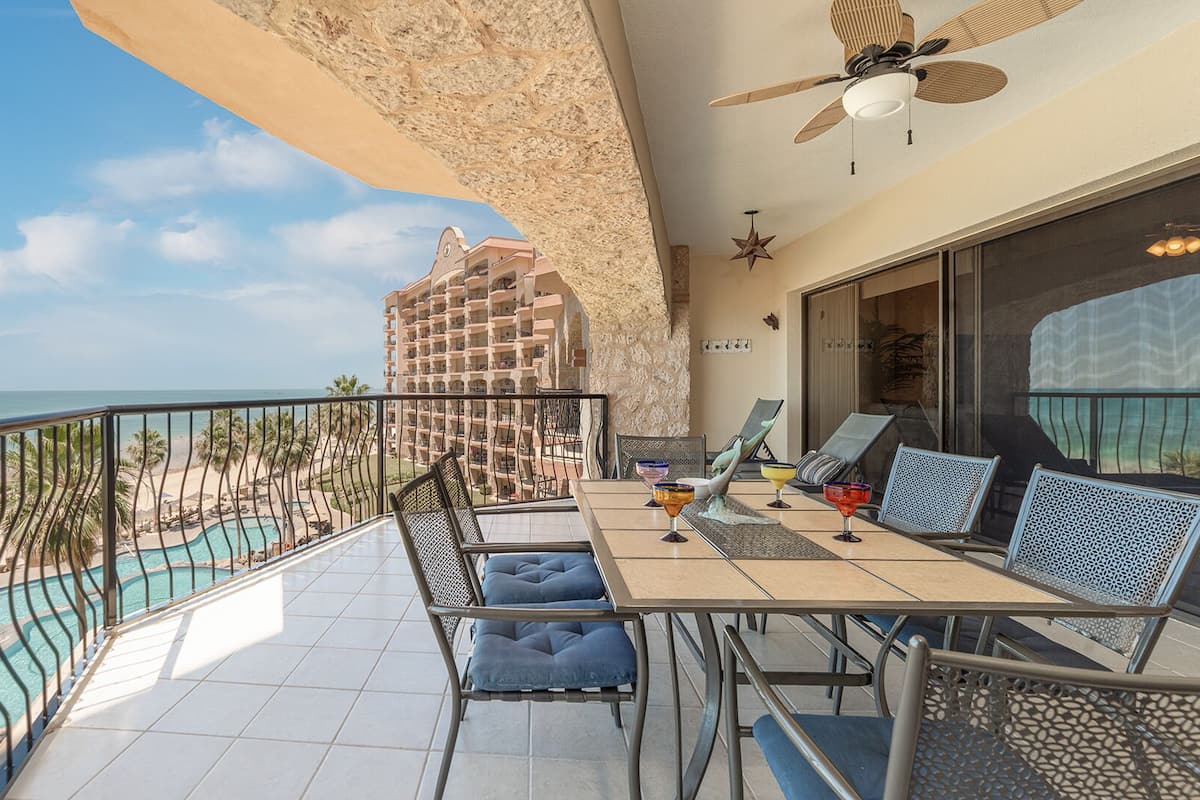 Een balkon met uitzicht op een zwembad, een eettafel met stoelen en een plafondventilator.