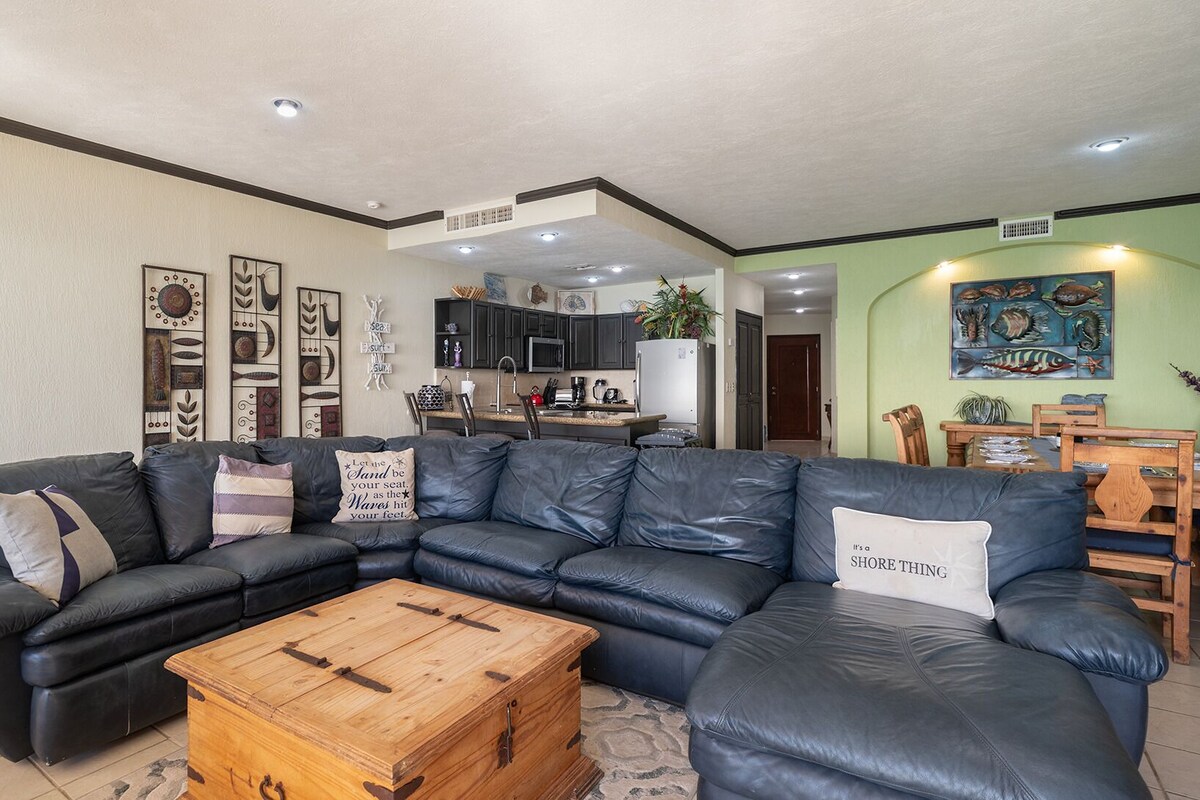 Ein modernes Wohnzimmer mit einem Ecksofa, einem Couchtisch aus Holz und einer Küche im Hintergrund.