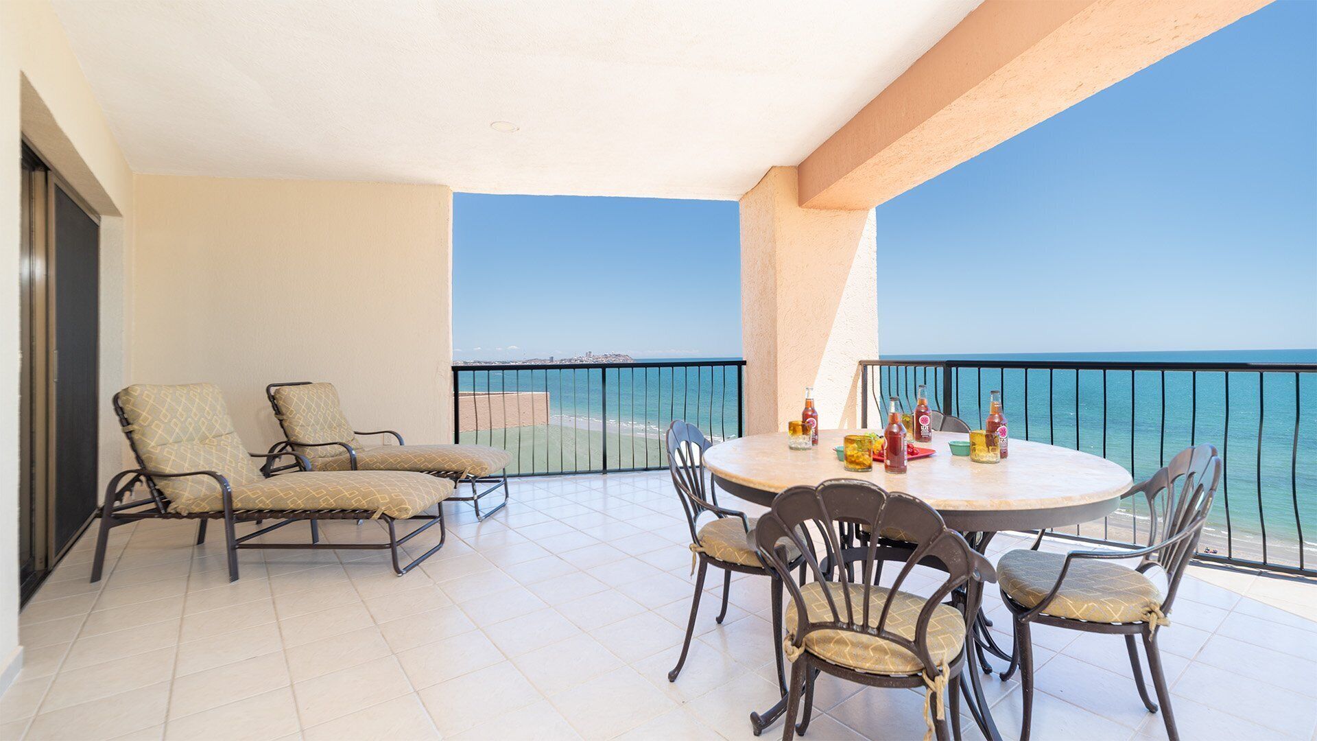 A balcony with a round table and chairs, a view of the sea, and a tiled floor.