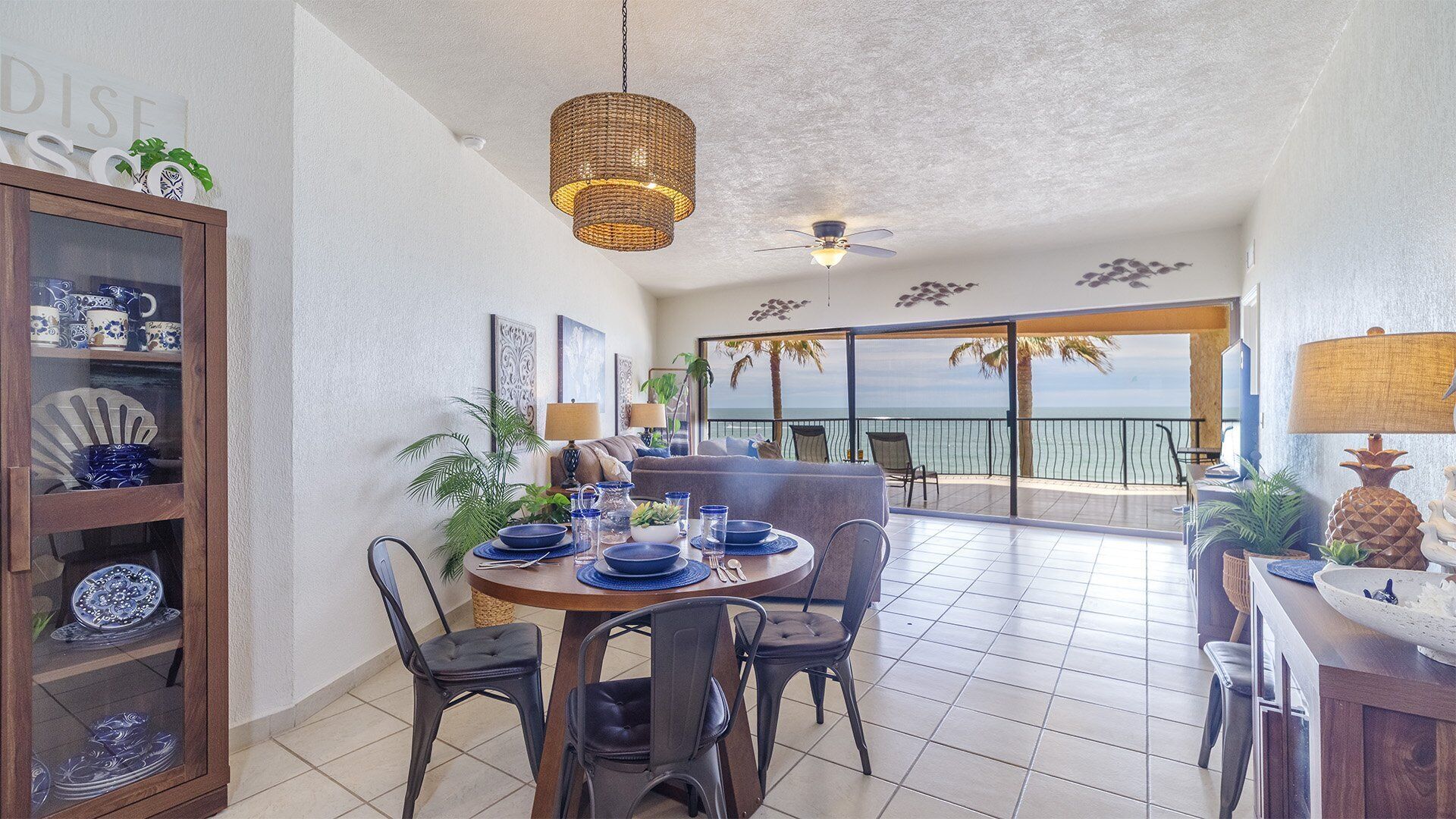 A dining area with a table set for four, surrounded by chairs, and a view of the ocean through a glass door.