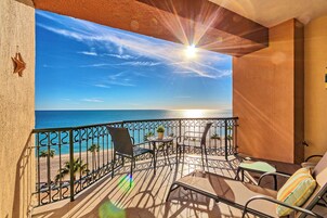 A balcony with a view of the sea, a table, chairs, and a small potted plant.