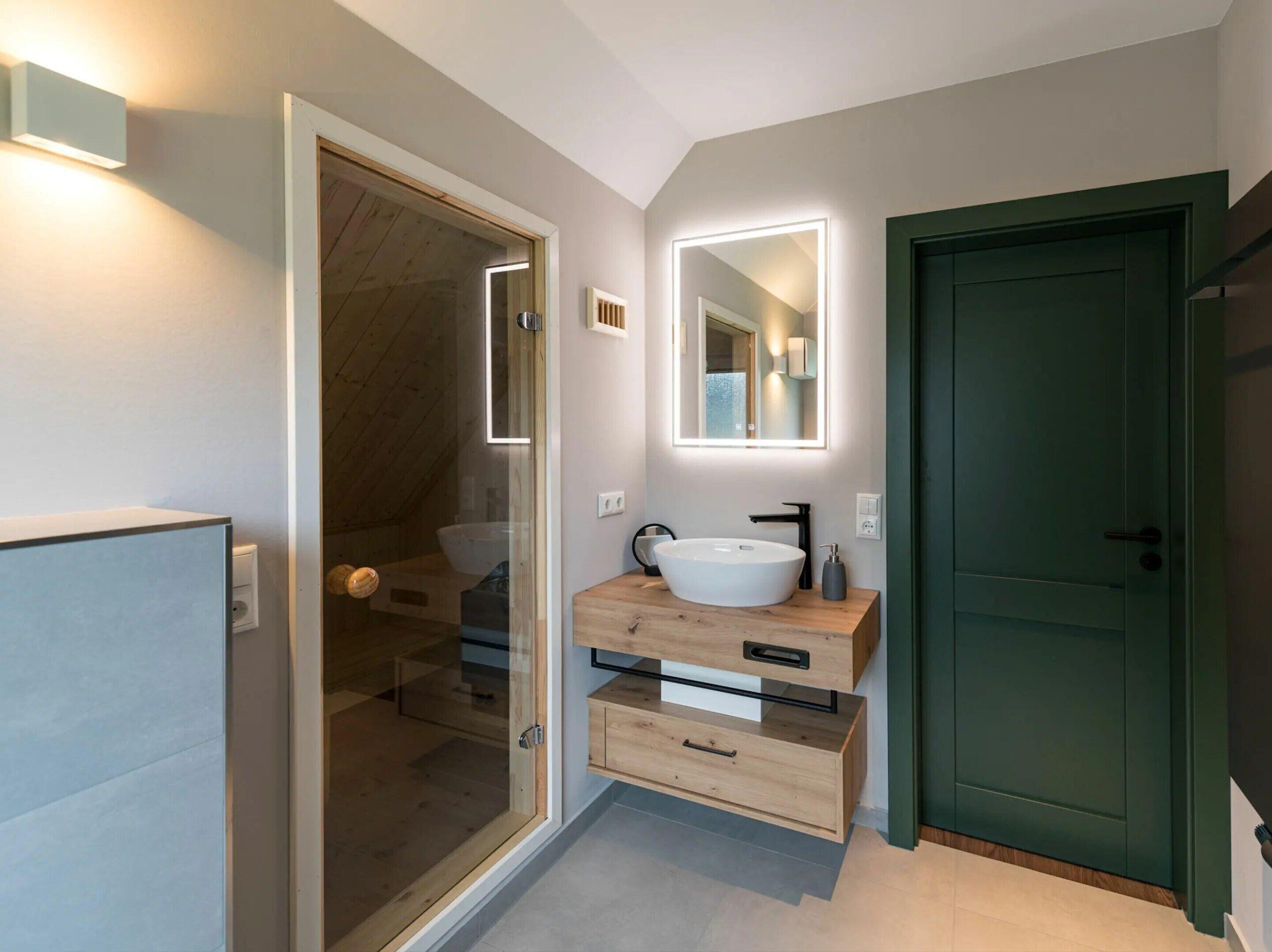 A modern bathroom with a glass shower enclosure, a wooden vanity with a large sink, and a green door.