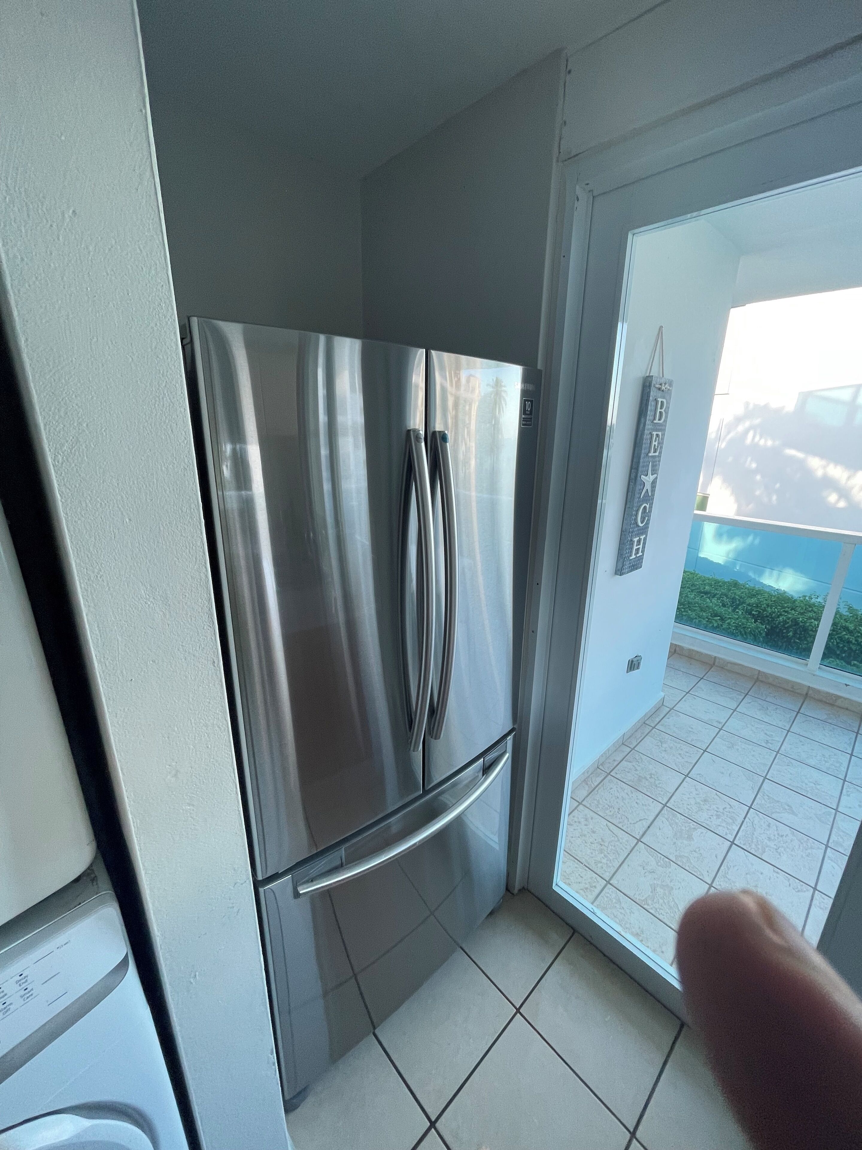 Un refrigerador de acero inoxidable en una cocina con piso de baldosas y vista a un balcón con barandilla.