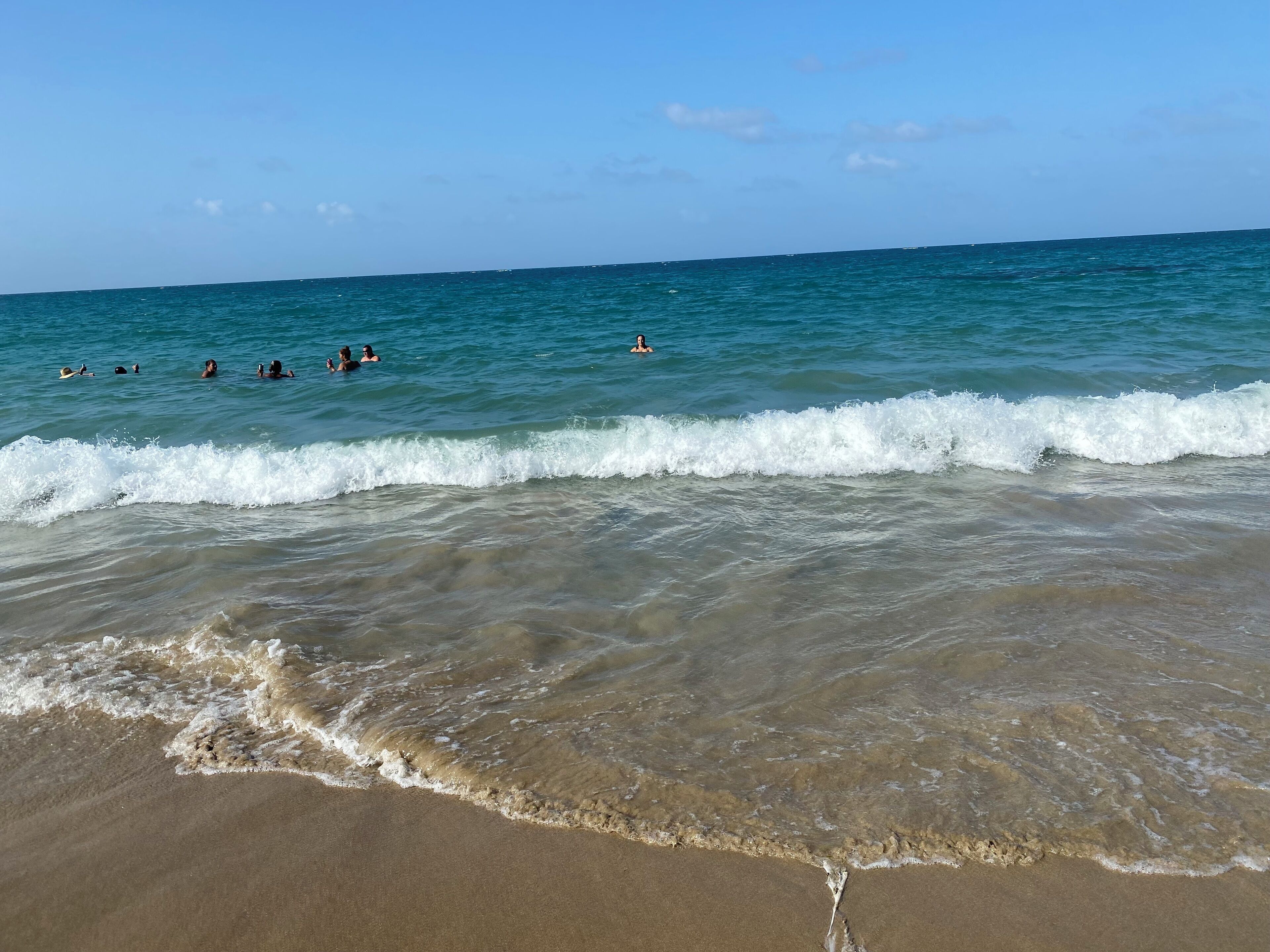 Ein Strand mit klarem Wasser, Wellen und badenden Menschen.