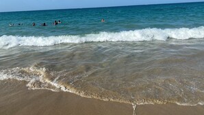 A beach with clear water, waves, and people swimming.