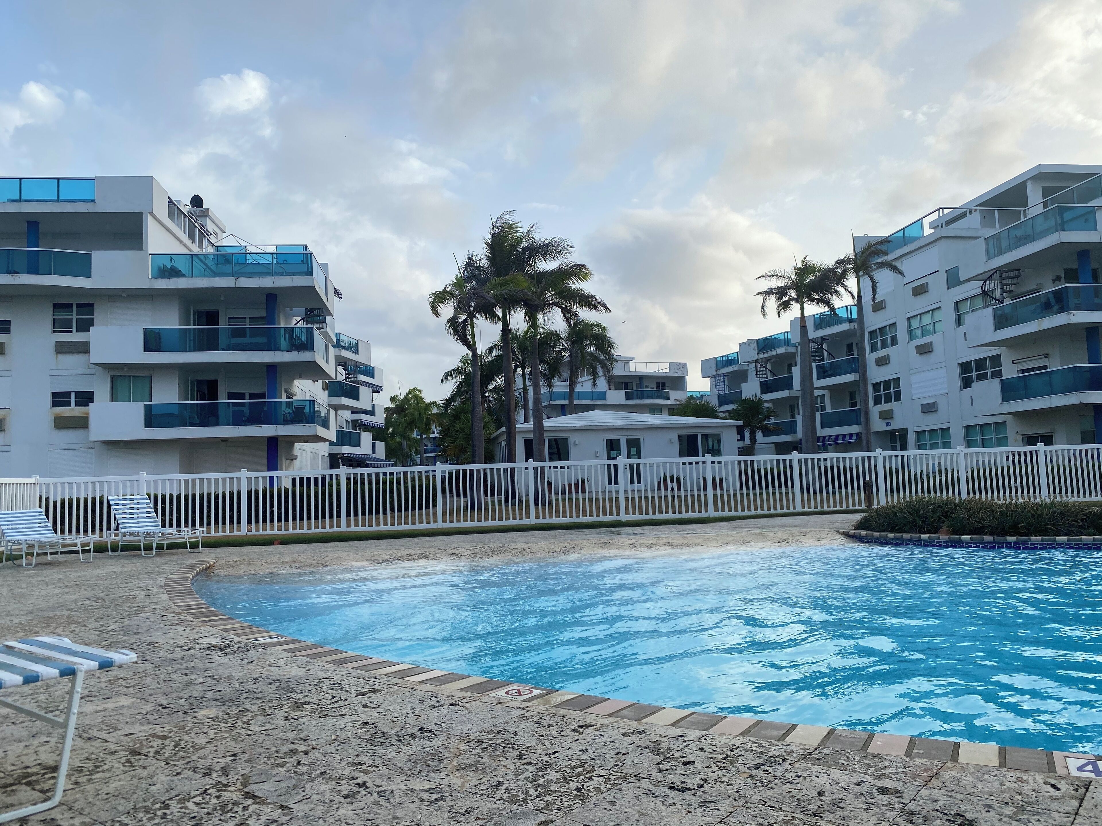 Ett modernt hotell med en swimmingpool, vita staket och palmer.