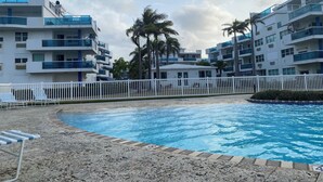 A modern hotel with a swimming pool, white fences, and palm trees.