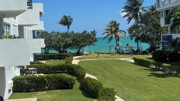 A resort with a clear view of the ocean, well-maintained lawns, and palm trees.