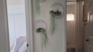 A hallway with three circular wall decorations containing plants, a bed with white bedding, and a wooden floor. - Minimalist Lake House (Helendale)