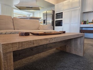 Een moderne keuken met witte kasten, een houten eettafel en een beige bank.